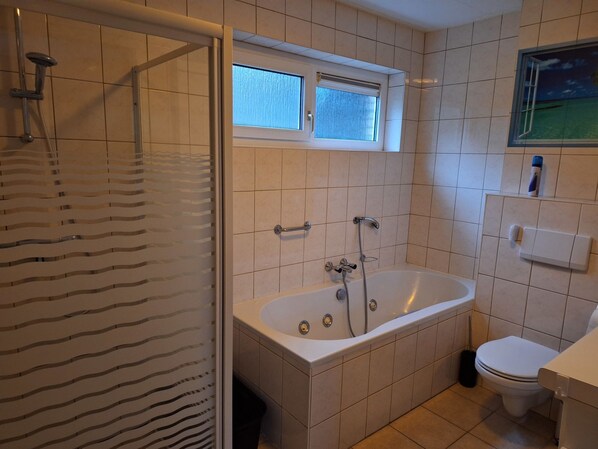 Une salle de bain avec une douche, une baignoire, des toilettes et une fenêtre.