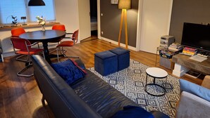 A modern living room with a black leather sofa, red and orange chairs, a dining table, a standing lamp, a TV, and a bookshelf. - Vacation home 4L by Interhome (Lochem)