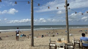Una playa con postes de madera, luces de cuerda y sillas.