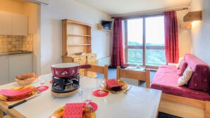 Een gezellige kamer met een eettafel gedekt voor twee personen, een bank, een televisie en een raam met gordijnen.