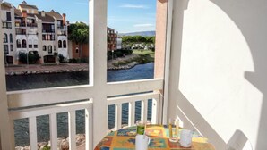 Un balcon avec une table dressée pour deux personnes, donnant sur une rivière et des bâtiments.