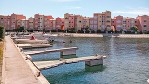 Un port de plaisance avec des bateaux amarrés, une promenade en béton et, au fond, des bâtiments roses dotés de balcons.