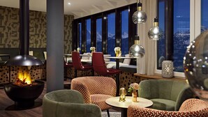 Een moderne lounge met een open haard, gestreept meubilair en grote ramen met uitzicht op de bergen.