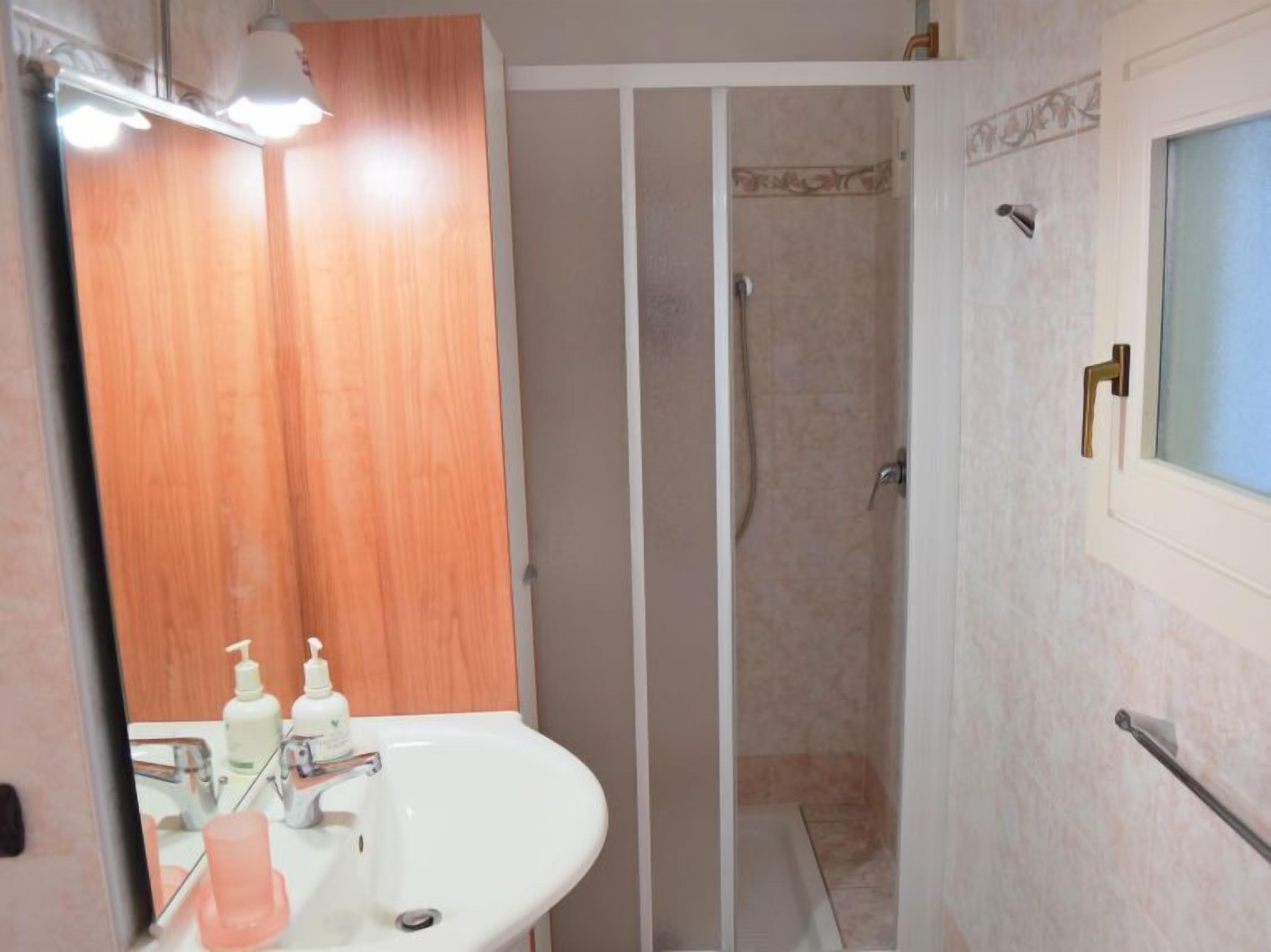 Une salle de bain avec un meuble-lavabo en bois, un lavabo blanc et une cabine de douche.