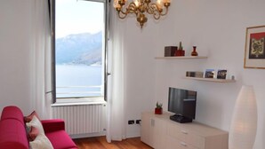 Een moderne woonkamer met een rode bank, een televisie op een wit kastje, en uitzicht op een meer door een raam.