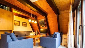 Un acogedor loft con techo de madera, un conjunto de sofás, un televisor y un ventanal grande.