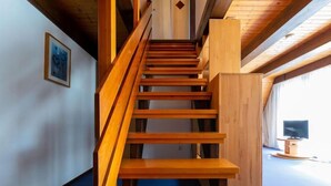 Una escalera de madera con piso cubierto de alfombra azul, que conduce a una habitación con un televisor.