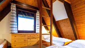 Un dormitorio acogedor en el ático con techo inclinado, literas de madera, una ventana con cortinas y un aparador de madera empotrado.