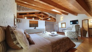 Ein Schlafzimmer mit einem großen Bett, einem Sessel, einem Fernseher und einer Holzbalkendecke.