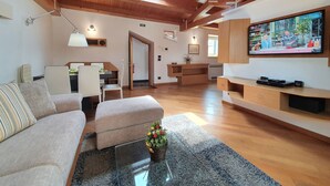 Ein geräumiges Wohnzimmer mit Holzboden, einer Couch, einem Couchtisch, einem Fernseher und einer Küchenzeile im Hintergrund.