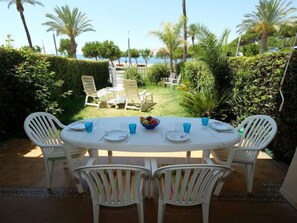 An outdoor dining area with a white table and chairs, surrounded by greenery and palm trees.