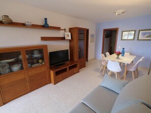 A living room with a TV, wooden cabinets, a dining table with chairs, and a sofa.