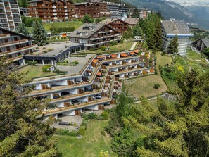 A modern hotel complex with multiple buildings, outdoor seating areas, and a mountainous backdrop.