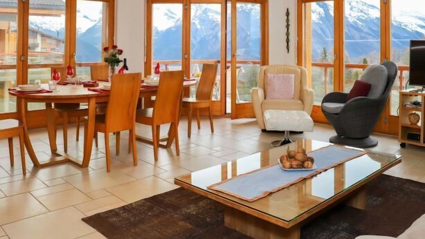 A spacious living room with a dining area, large windows with mountain views, a comfortable sofa, and a television. - Domaine des Reines C10 by Interhome (Nendaz)