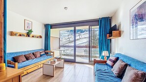 Een woonkamer met twee blauwe banken, een houten salontafel en een televisie op een standaard.