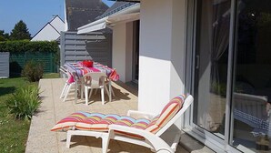 Un patio con tavolo e sedie, una poltrona relax e una porta scorrevole in vetro.