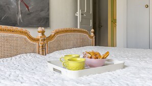 A bed with a decorative headboard, a tray with yellow mugs and a bowl of pastries, and a painting on the wall. - Le Concordia by Interhome (Nice)