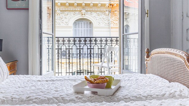 A hotel room with a balcony, a bed with a white textured blanket, a small table with a tray of pastries, and a Mickey Mouse poster on the wall. - Le Concordia by Interhome (Nice)