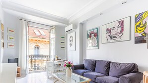 A modern living room with a purple sofa, a glass coffee table, and a balcony with a view of a building with orange facades. - Le Concordia by Interhome (Nice)