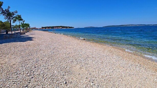 A pebble beach with clear blue water, a distant island, and a few trees. - Apartment Ante by Interhome (Brodarica)