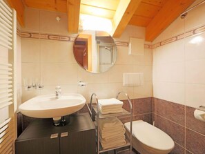 Une salle de bain avec un miroir rond, un lavabo, des toilettes et un porte-serviettes.