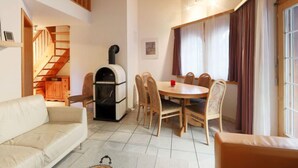 Ein gemütliches Wohnzimmer mit Kamin, einem Essbereich mit Holzsesseln, einer Couch und einer Treppe, die zu einer oberen Ebene führt.