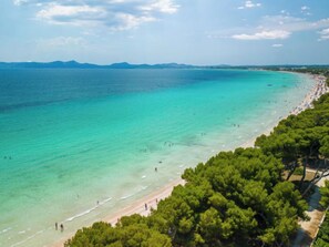 Een kuststrand met helder turquoise water, een zandstrand en dichte groene bomen.