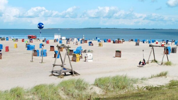 Een strand met veel kleurrijke strandhuisjes en een grote blauwe ballon in de verte.