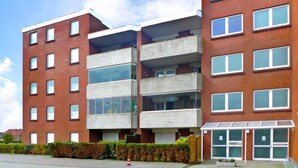 Een meerhoog gebouw met een gevel van baksteen en beton, grote ramen en een hekwerk.