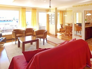 A living room with a sofa, a coffee table, and four armchairs. There is a dining area with a table and chairs in the background.