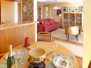 A cozy living room with a red sofa, a dining table with a candle, and a kitchen area with a tiled backsplash.