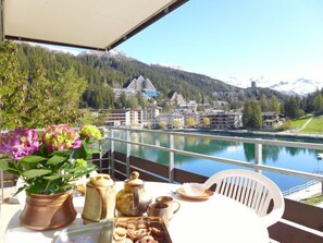 Ein Balkon mit einem für Tee gedecktem Tisch, mit Blick auf einen See und eine bergige Stadt.