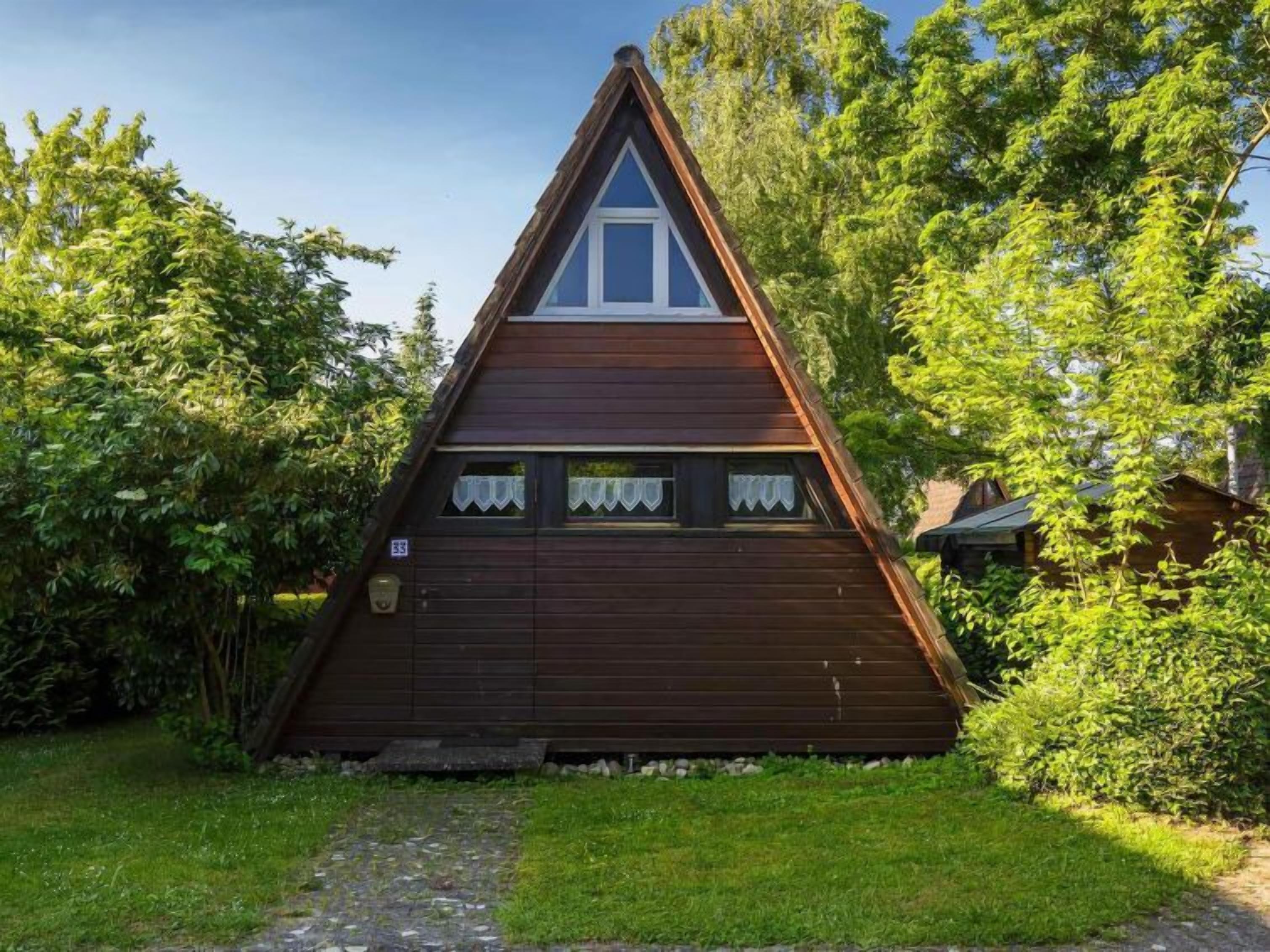 Eine dreieckige Holzhütte mit spitzem Dach, umgeben von üppigem Grün.