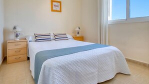 A bedroom with a bed, two bedside tables, a nightstand, a window, and a framed picture on the wall. - Bahia Blanca by Interhome (Dénia)