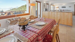 A dining area with a checkered tablecloth, wooden chairs, and a view of a mountainous landscape through large windows.