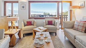 A cozy living room with two sofas, a coffee table, and a view of mountains through large windows.