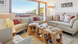 A cozy living room with a sofa set, a coffee table, and a view of mountains through large windows.