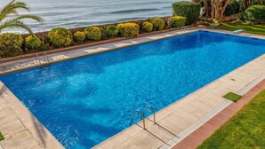 A rectangular swimming pool with clear blue water, surrounded by a tiled deck and a low stone wall.