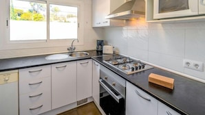 A modern kitchen with a gas stove, a microwave, and a sink. There is a window providing natural light and a view of greenery outside.