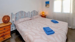 A bedroom with a bed, a nightstand with a lamp, a dresser, and a window with curtains.