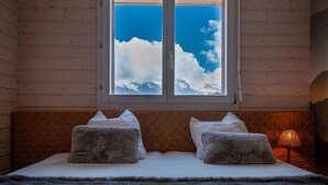 A bed with two pillows, a window with a view of snow-capped mountains, and a lamp on the right. - Les Chouettes 23 by Interhome (Nendaz)