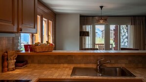 A kitchen with a built-in sink, wooden cabinets, a window with a view of a building, and a hanging light fixture. - Les Chouettes 23 by Interhome (Nendaz)