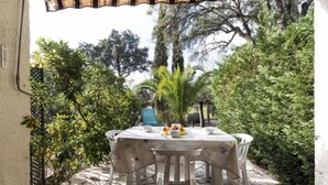 An outdoor patio with a table set for two, surrounded by lush greenery and trees. - Val des Chênes by Interhome (Cavalaire)