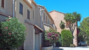 A row of Mediterranean-style buildings with stucco walls and terracotta roofs, surrounded by lush greenery and a clear blue sky. - Val des Chênes by Interhome (Cavalaire)