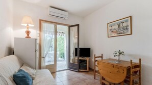 A cozy room with a sofa, a wooden dining table with chairs, a TV, and an air conditioning unit. - Val des Chênes by Interhome (Cavalaire)