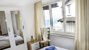 Ein Hotelzimmer mit einem großen Spiegel, einem Bett mit zwei Kissen, einem kleinen Tisch mit einer Ananas und Blick auf ein Gebäude durch das Fenster.