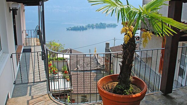 Ein Balkon mit einem Topfpalmen und Blick auf einen See sowie eine entfernte Insel.