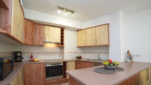 Une cuisine avec des meubles de rangement en bois, un four encastré, un évier et un panier de fruits posé sur le plan de travail.