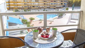 Un balcon avec une table préparée pour le petit-déjeuner, donnant sur une piscine et sur le paysage urbain.