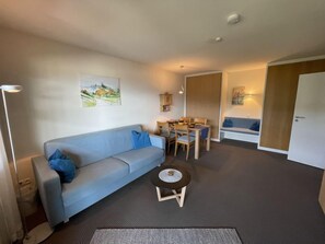 A living room with a sofa, a coffee table, a dining table with chairs, and a painting on the wall.